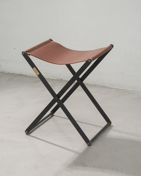 Foldable stool with brown leather seat and black metal frame on a white floor.