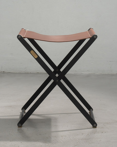 Folding stool with pink leather seat and black metal frame on a gray background