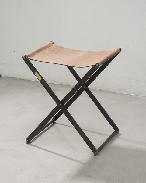 Foldable stool with leather seat on a white floor and wall