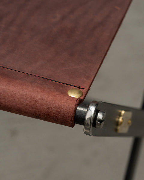 Close-up of a brown leather strap with stitching and metal hardware on a gray surface.