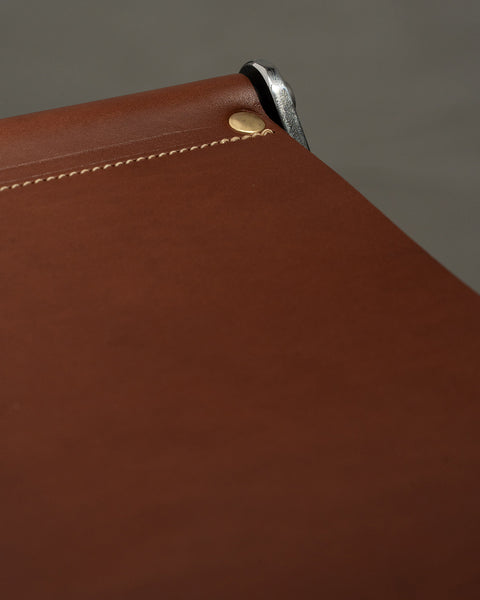Close-up of a brown leather product with stitching detail on a gray background