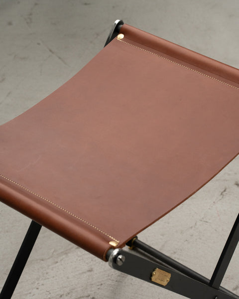 Brown leather stool with black metal legs on a concrete floor.