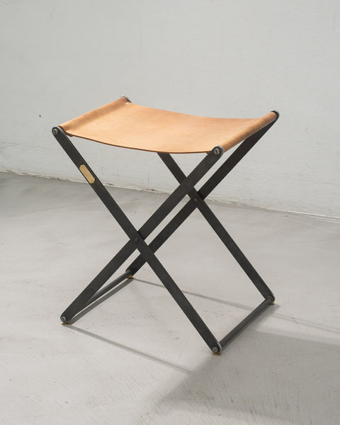 Folding stool with leather seat on a white floor and wall