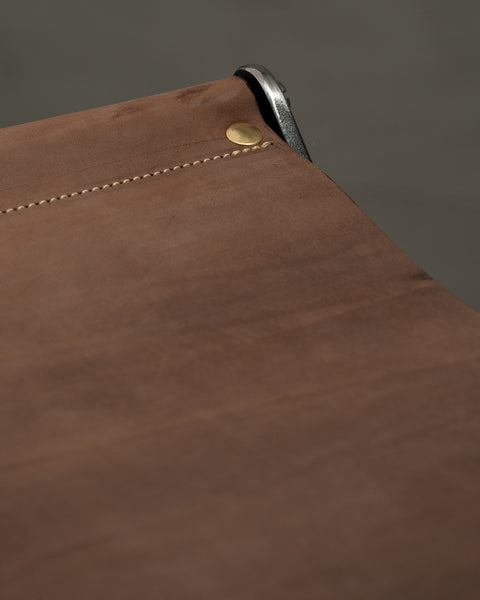 Close-up of a brown leather product with stitching detail on a gray background